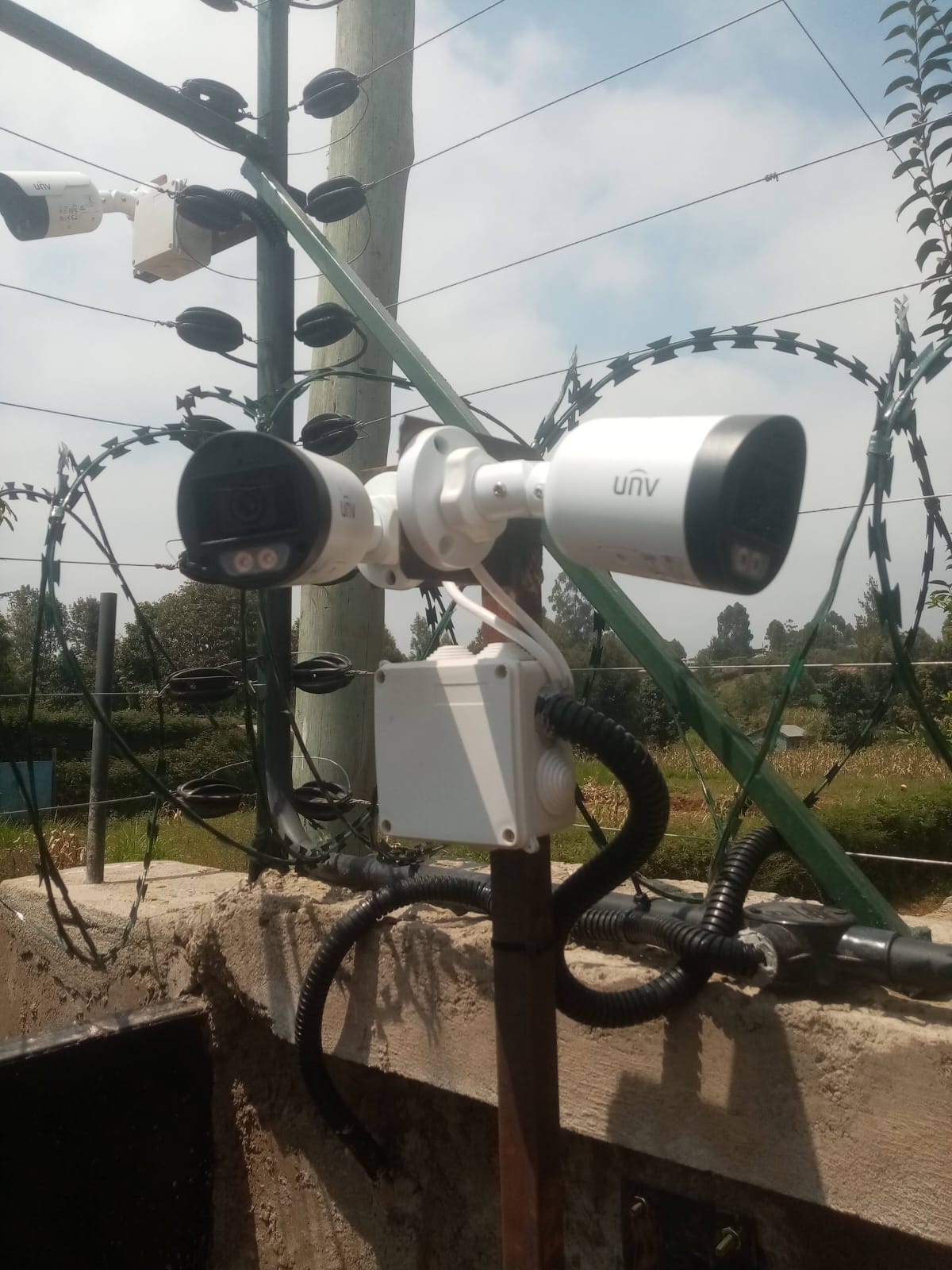 Two Uniview bullet CCTV cameras mounted on a shared bracket on an electric fence post in Kikuyu, razor wire visible