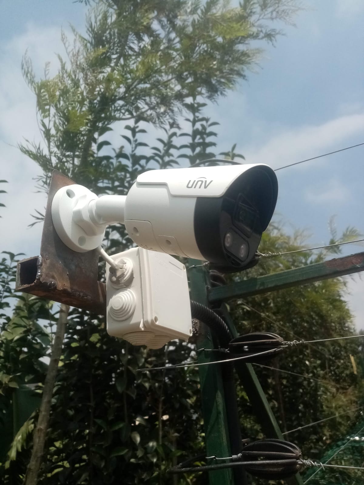 Close-up of a Uniview bullet CCTV camera mounted on a steel bracket integrated with an electric fence post in Kikuyu