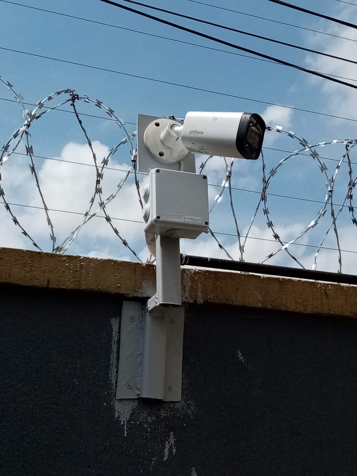 Close-up of Dahua bullet CCTV camera and junction box mounted on a galvanised pole above razor wire coils, Muthaiga