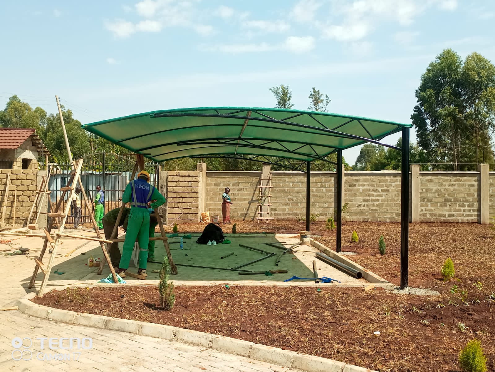 Finished curved green tensile-roof car parking shade structure in a landscaped garden setting in Bungoma