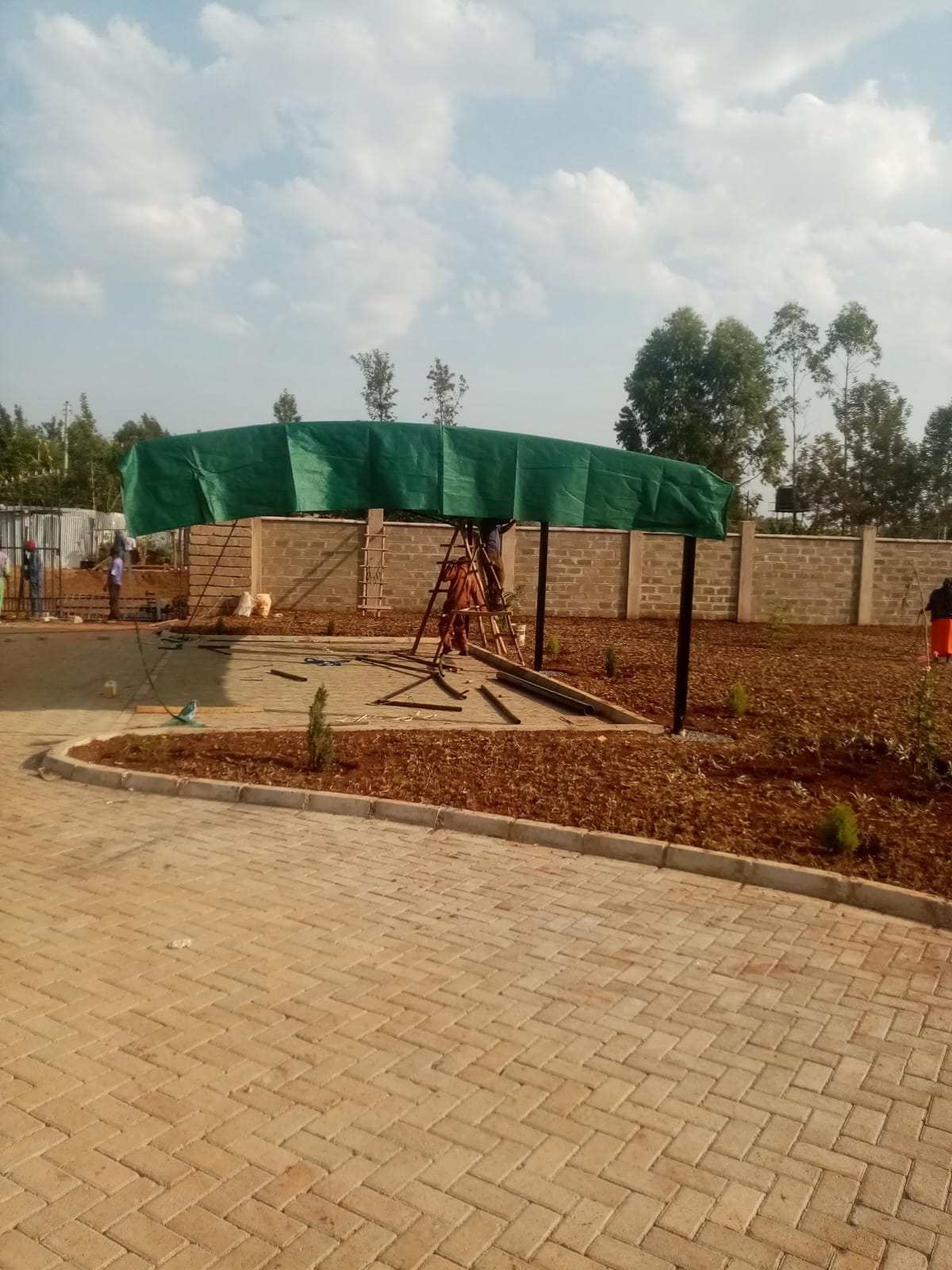 Green tensile shade fabric being pulled over a curved steel frame during car parking shade installation in Bungoma