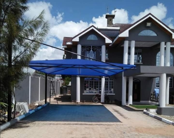 Blue cantilever car parking shade structure covering the paved forecourt of a modern double-storey house in Kileleshwa