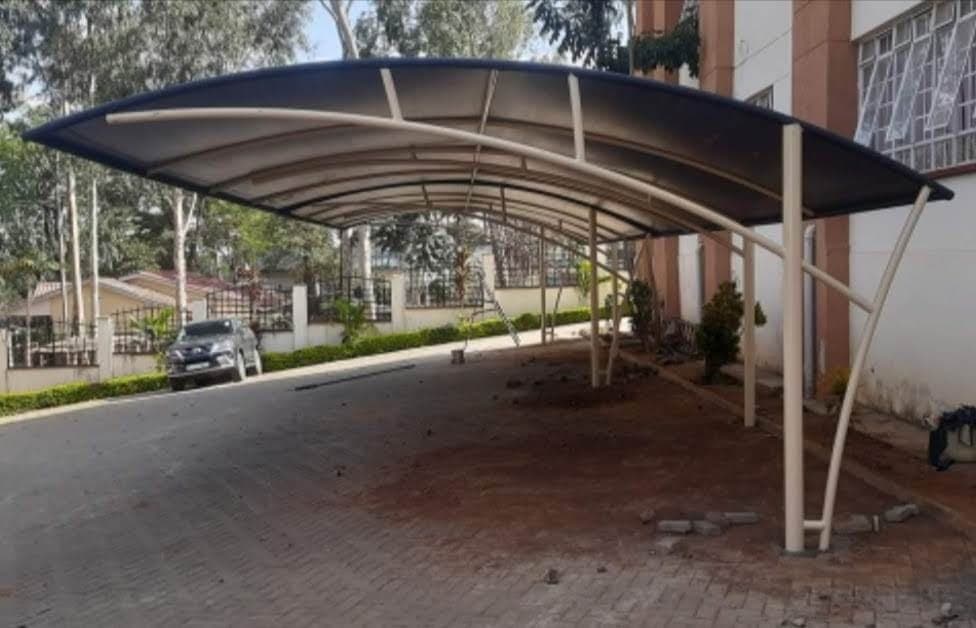 Finished curved cream tensile-roof car parking shade structure with an arched steel frame at a property in Makueni