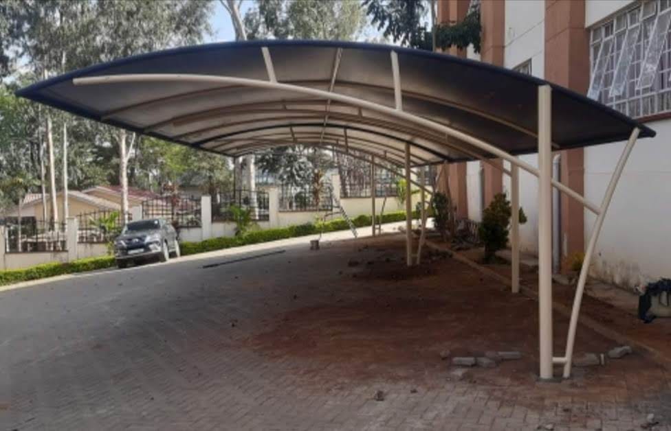 Finished curved cream tensile-roof car parking shade structure with an arched steel frame at a property in Makueni
