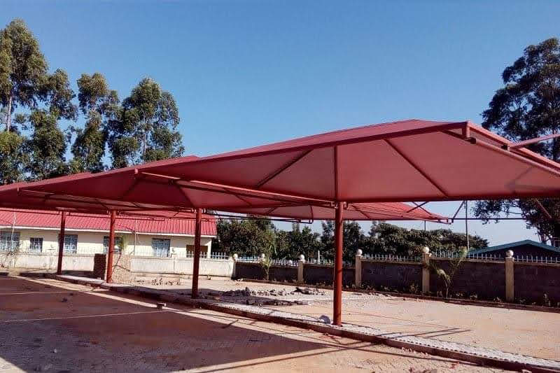 Red tensile cantilever car parking shade structure installed alongside a dormitory-style building in Nairobi
