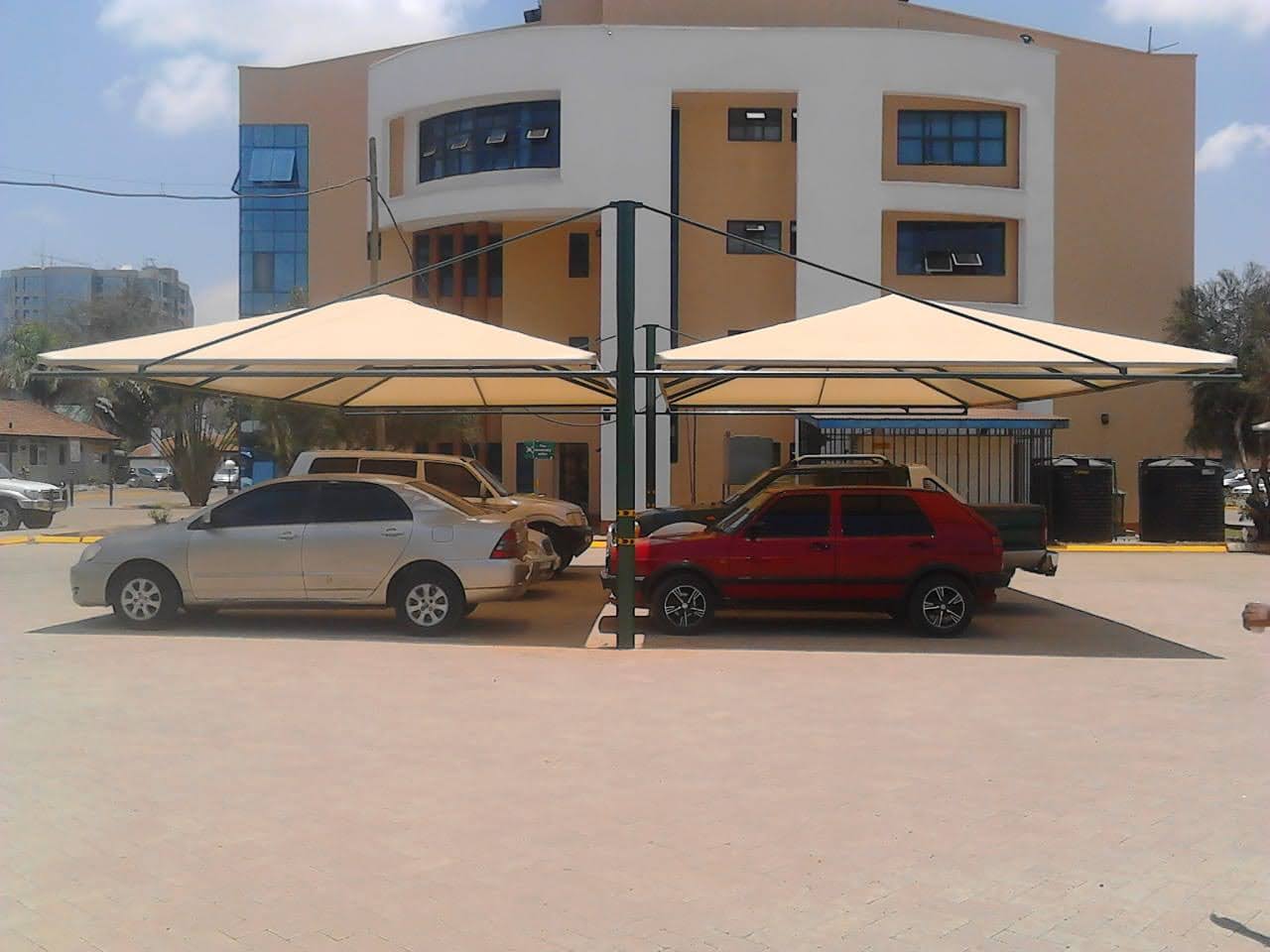 Twin cream umbrella-style car parking shade structures covering multiple bays in front of a curved multi-storey building in Nairobi