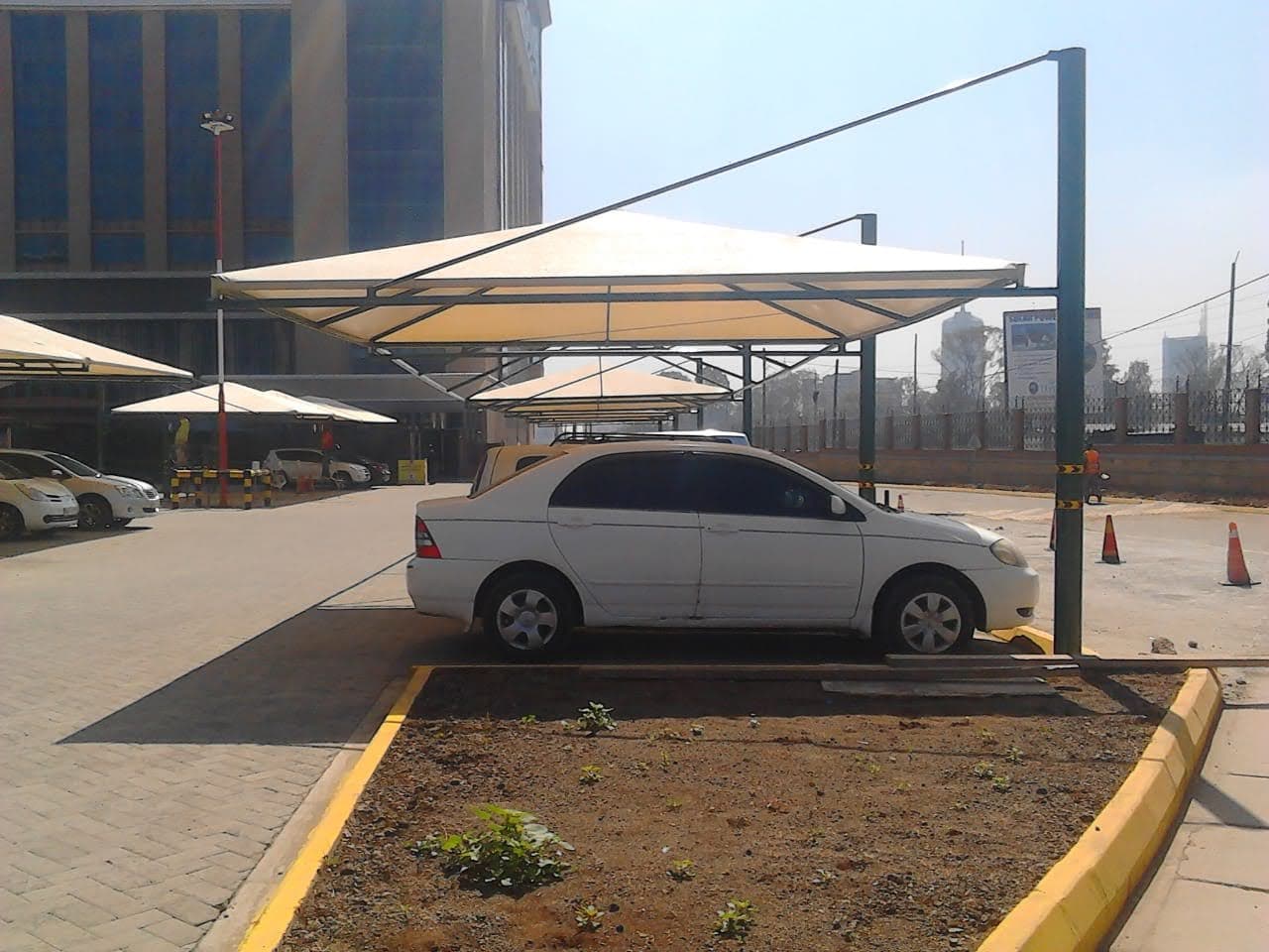 Row of cream umbrella-style car parking shade structures covering a commercial building forecourt in Nairobi