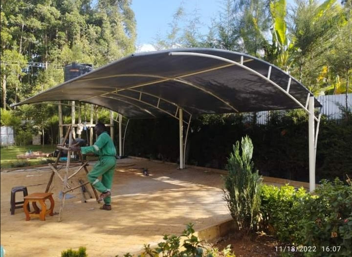 Curved cream tensile-roof car parking shade structure under construction at a property in Naivasha, technician fitting fabric to the arched steel frame
