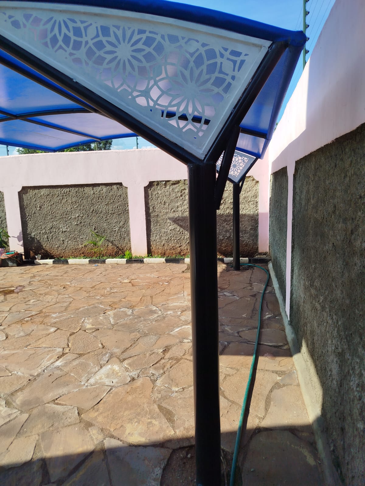Close-up of a laser-cut floral pattern panel insert at the corner joint of a blue car parking shade structure in Runda