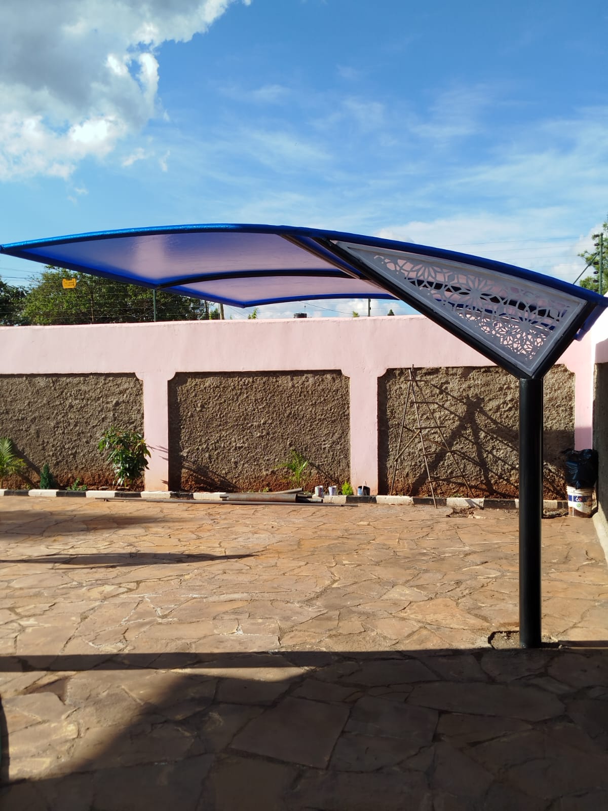 Side view of a designer car parking shade with laser-cut panel detail at a Runda property, decorative pink boundary wall behind