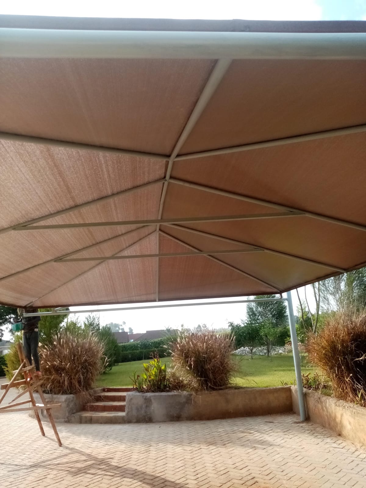 Underside view of a finished maroon tensile cantilever car parking shade structure in Thika, showing steel cross-bracing