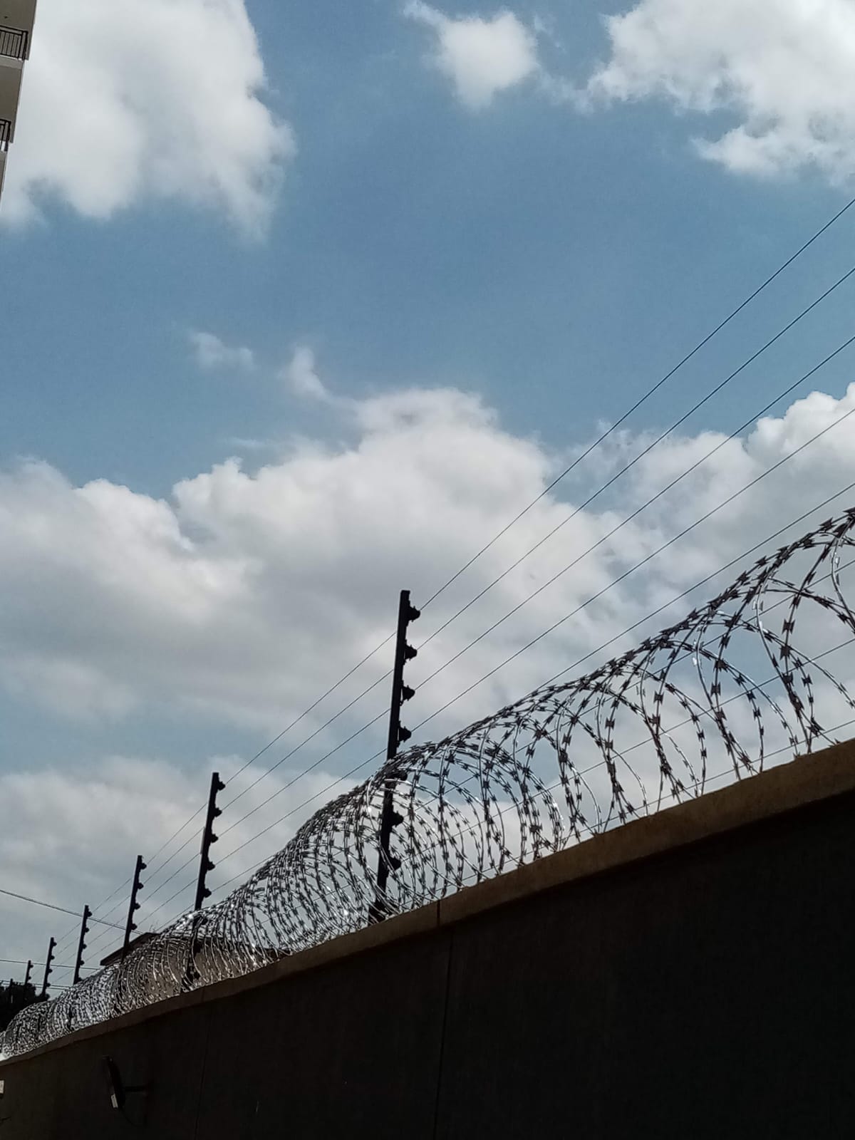 Electric fence posts and razor wire along a boundary wall at a Limuru apartment complex, wide view