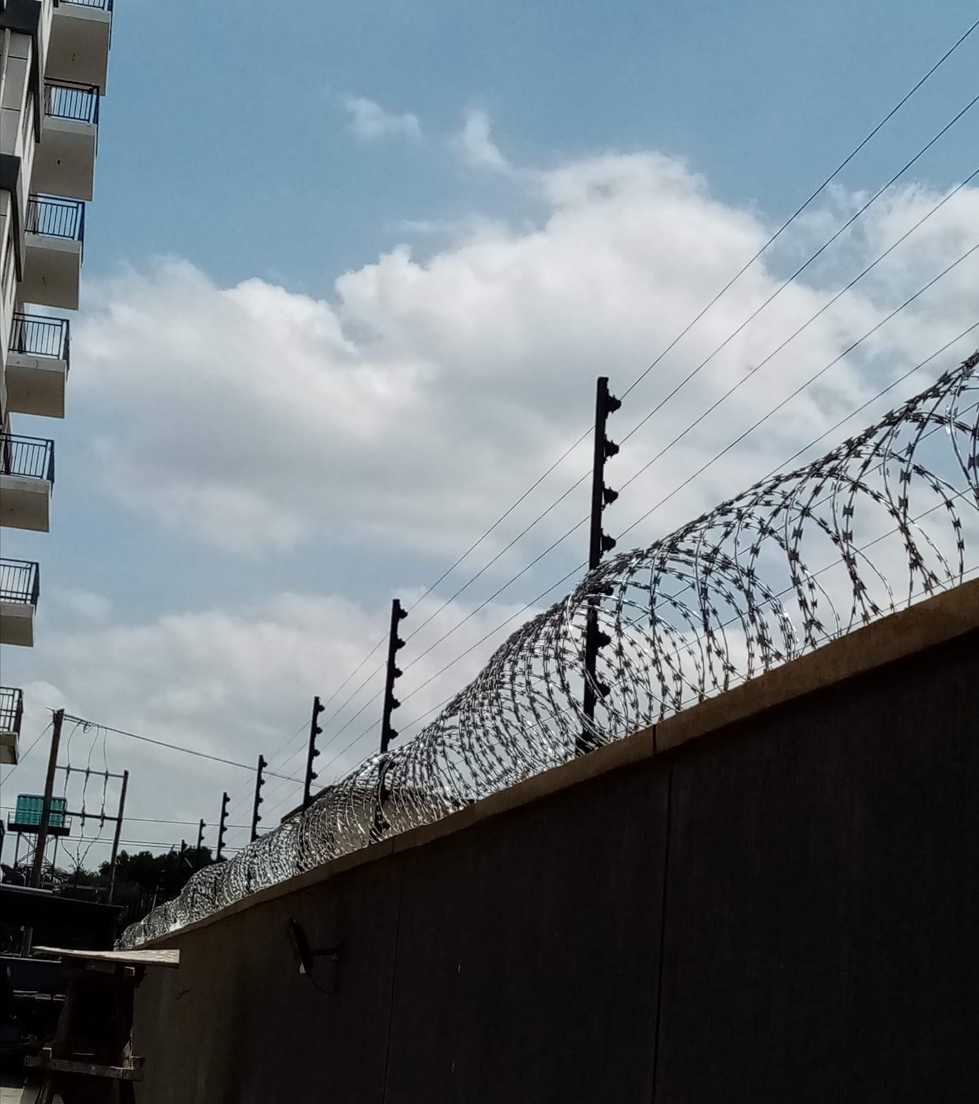 Electric fence and razor wire perimeter wall with apartment blocks visible behind, Limuru