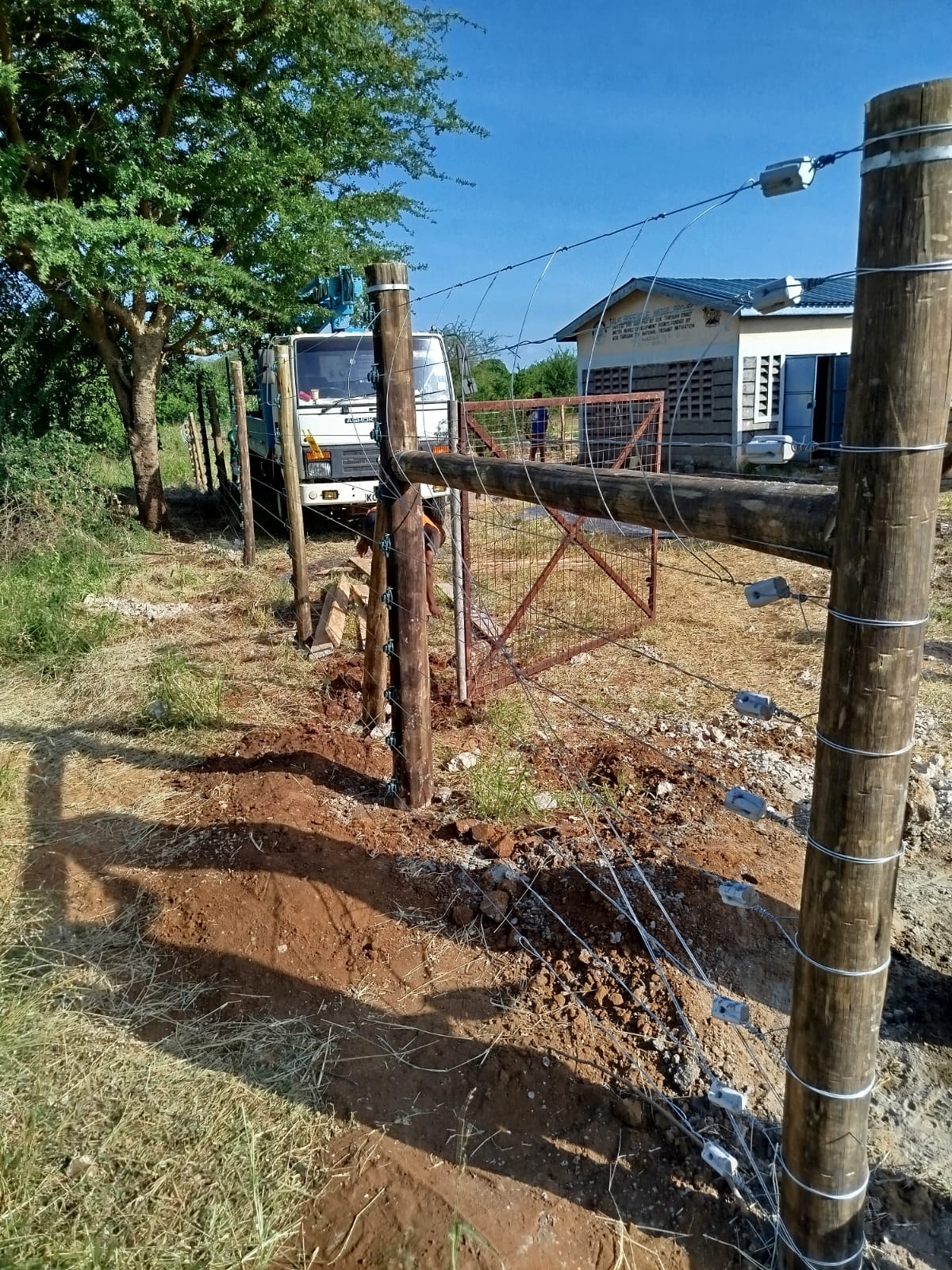Technicians installing timber electric fence posts near a crane truck at a site in Emali