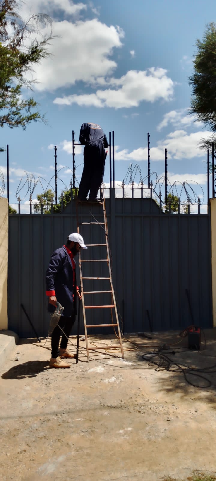Technicians fitting electric fence posts and razor wire along the top of a gate structure in Nanyuki