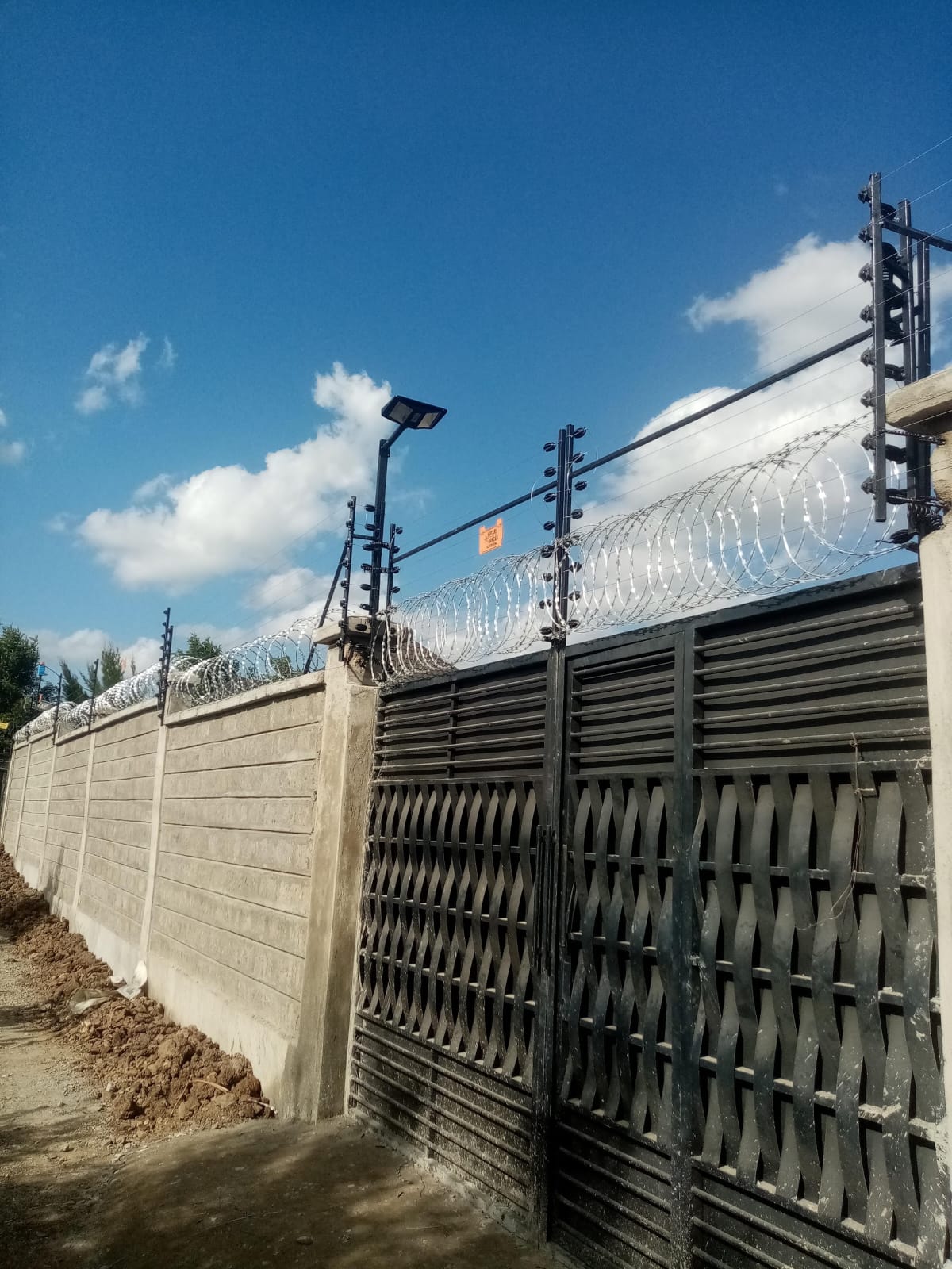 Electric fence and razor wire integrated across a decorative steel gate at a Ruiru property, wide view