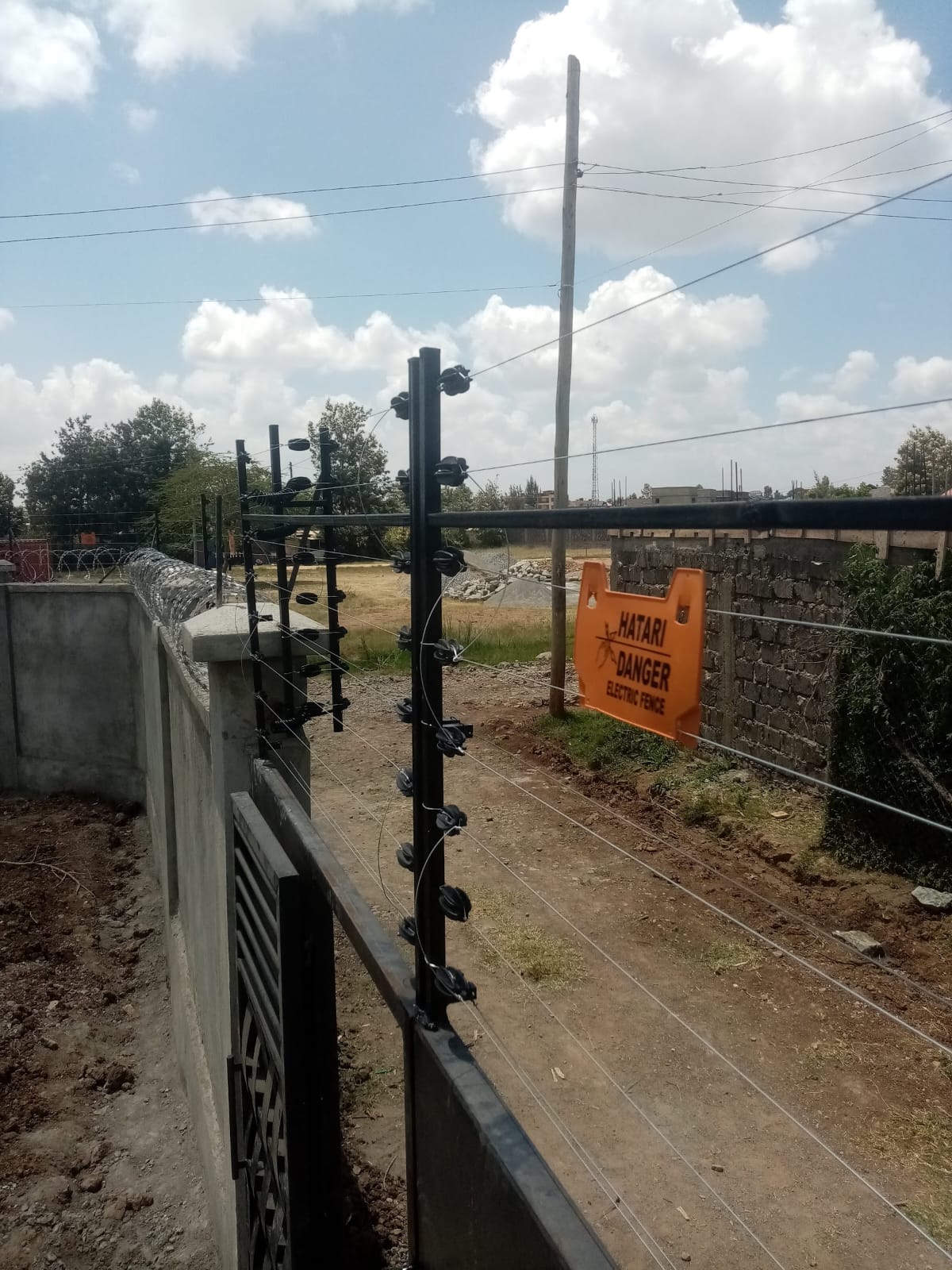 Electric fence post with an orange 'Hatari Danger' warning sign along a newly built boundary wall in Ruiru