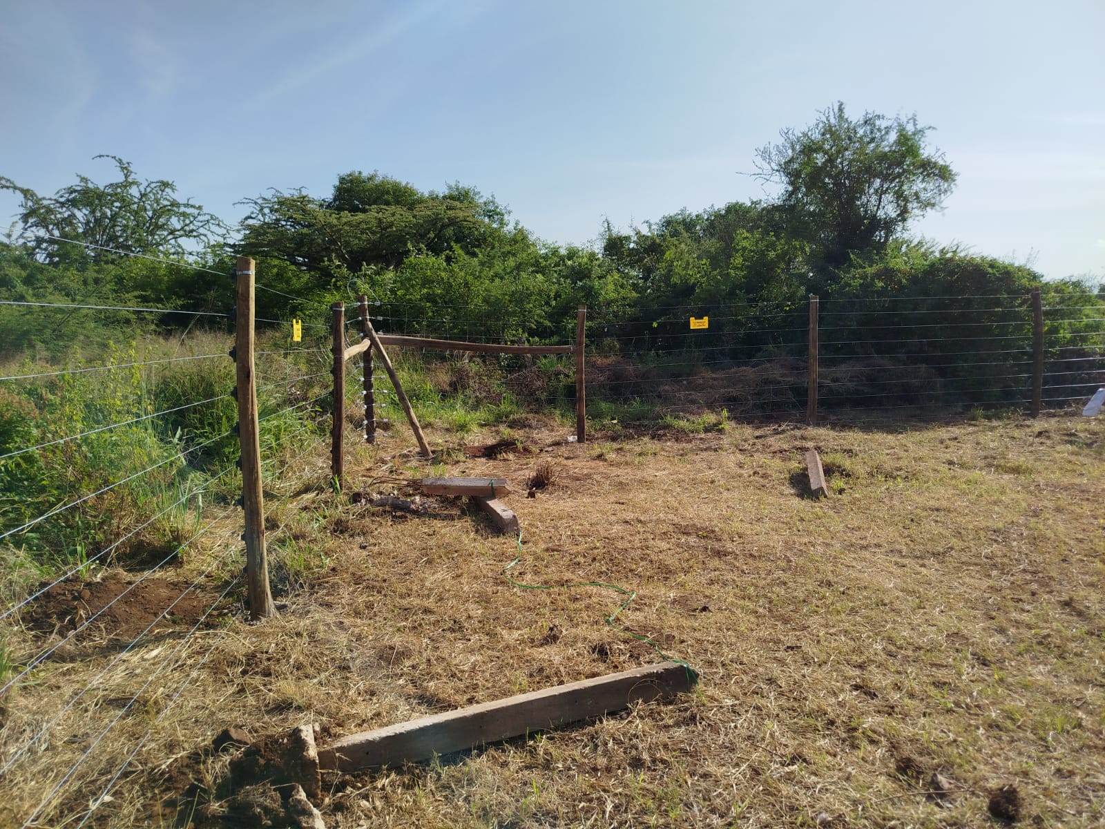 Wide view of electric fence posts and wire strands along a boundary near Voi, Tsavo hills in the background