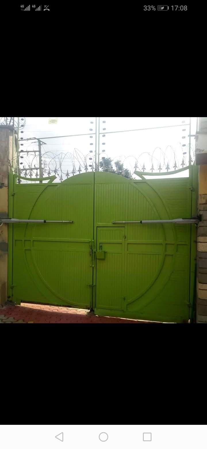 Bright green double-leaf swing gate with dual arm motors, topped with razor wire and electric fence wires, Kakamega