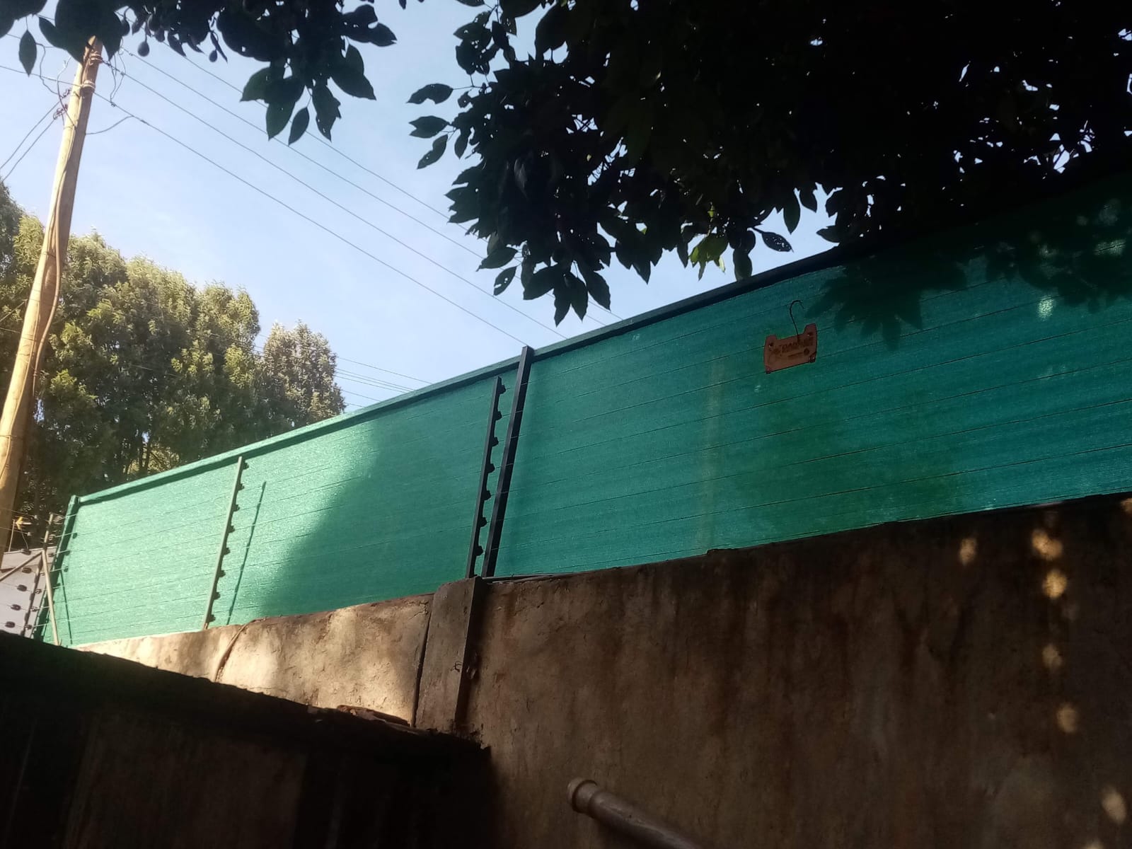 Green privacy shade net combined with electric fence wire strands along a boundary wall in Kiambu, wide view