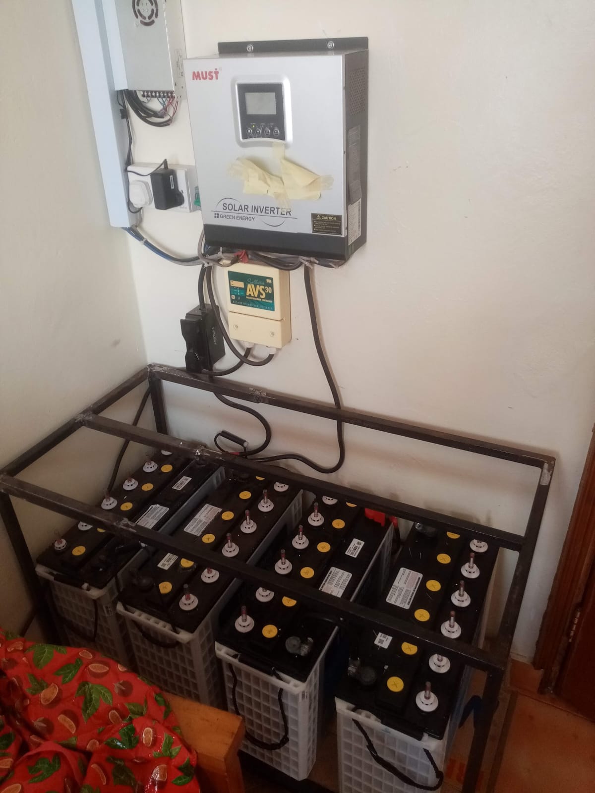 MUST solar hybrid inverter and AVS30 charge controller wall-mounted above a battery rack in a Kiambu home