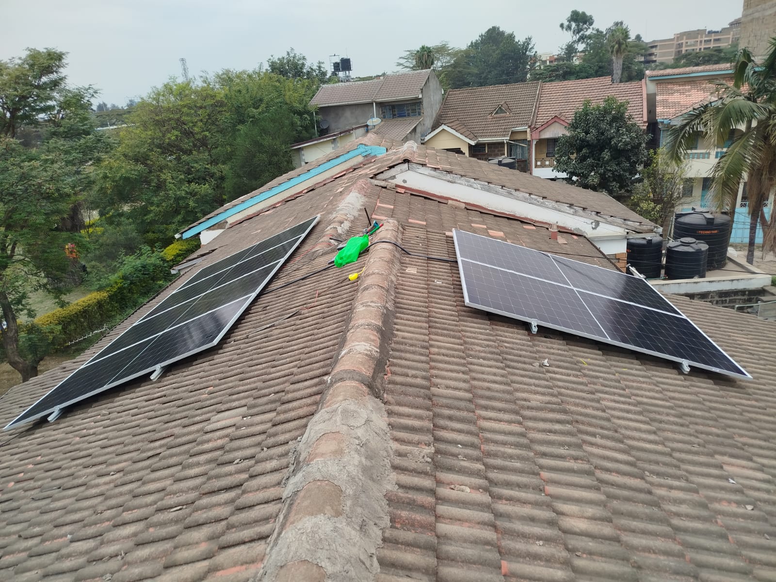 Solar panels mounted on a tiled roof across a Nairobi apartment complex, surrounding rooftops and water tanks visible
