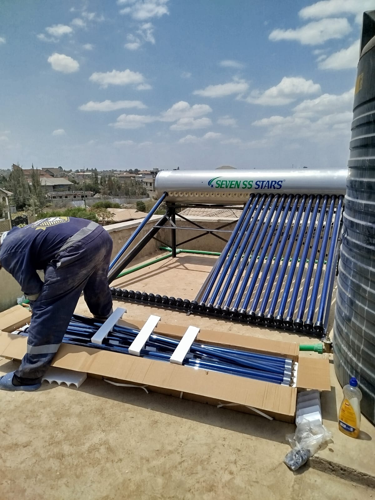 Technician fitting evacuated collector tubes to a solar water heater frame on a rooftop in Katani