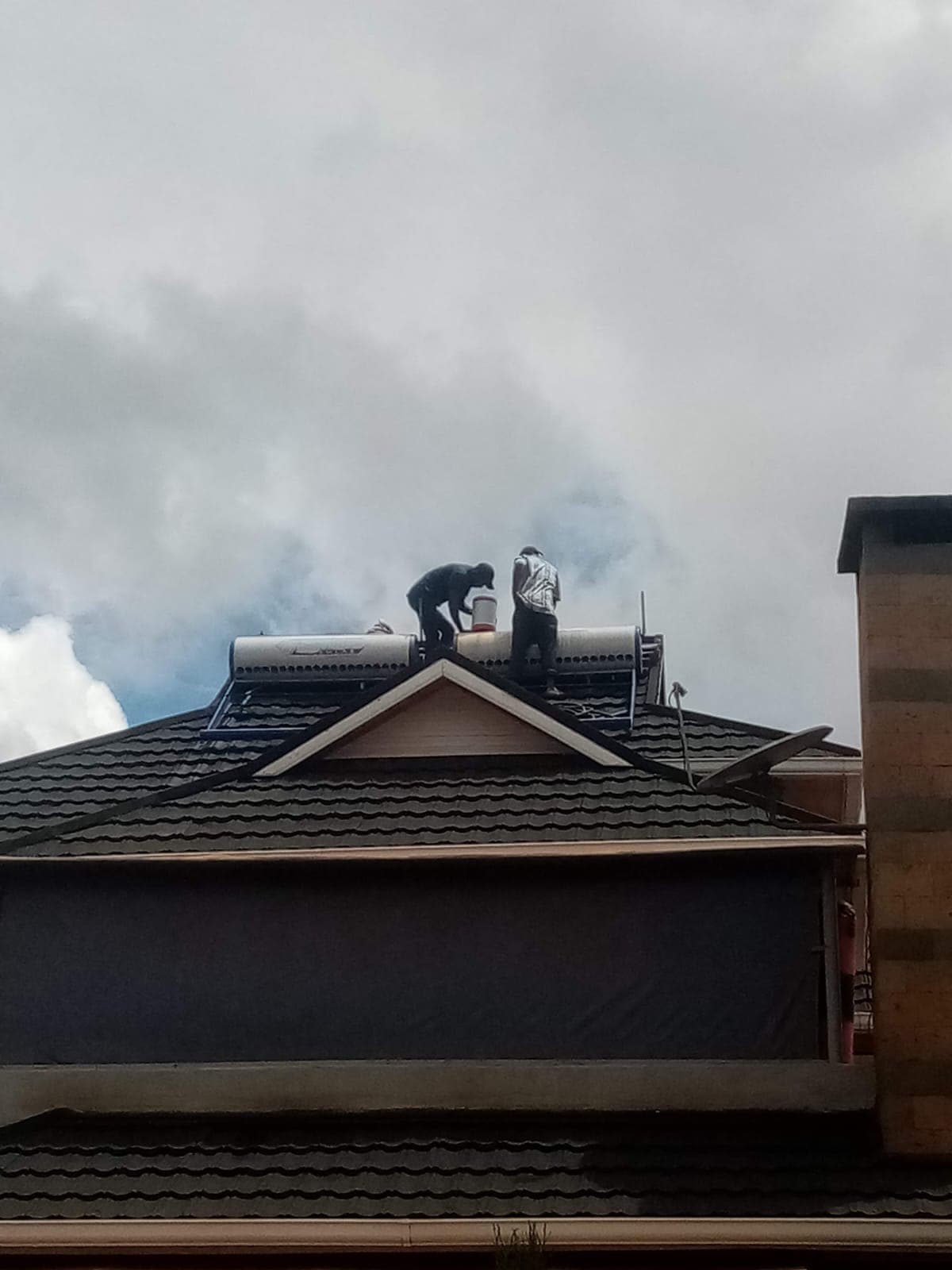 Two evacuated-tube solar water heater tanks installed side by side on a tiled rooftop in Kiambu, hills visible in the background