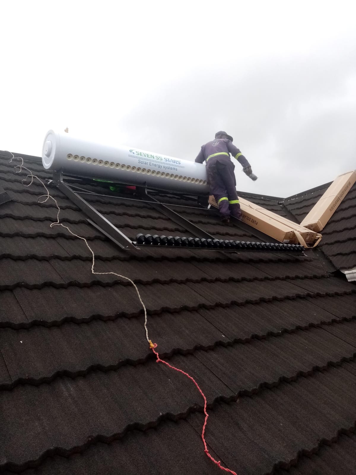 Technician positioning the tank of a 350L solar water heater on a tiled roof in Kisumu, boxed collector tubes alongside