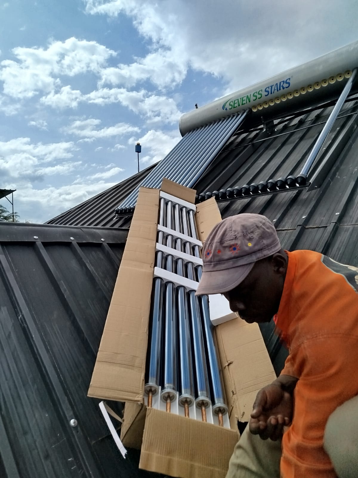 Technician handling boxed collector tubes during solar water heater installation in Nyahururu, alternate angle