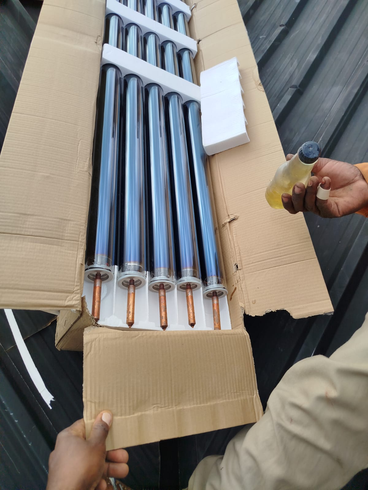 Technician adding heat transfer fluid to evacuated collector tubes during solar water heater installation in Nyahururu